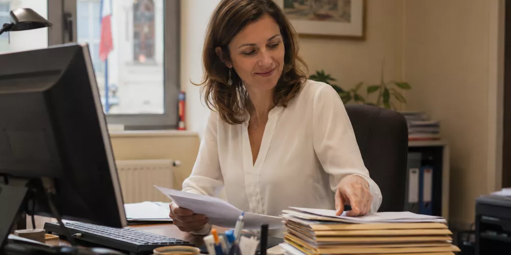 Secrétaire de mairie traitant des courriers et dossiers administratifs dans un bureau de collectivité territoriale moderne.