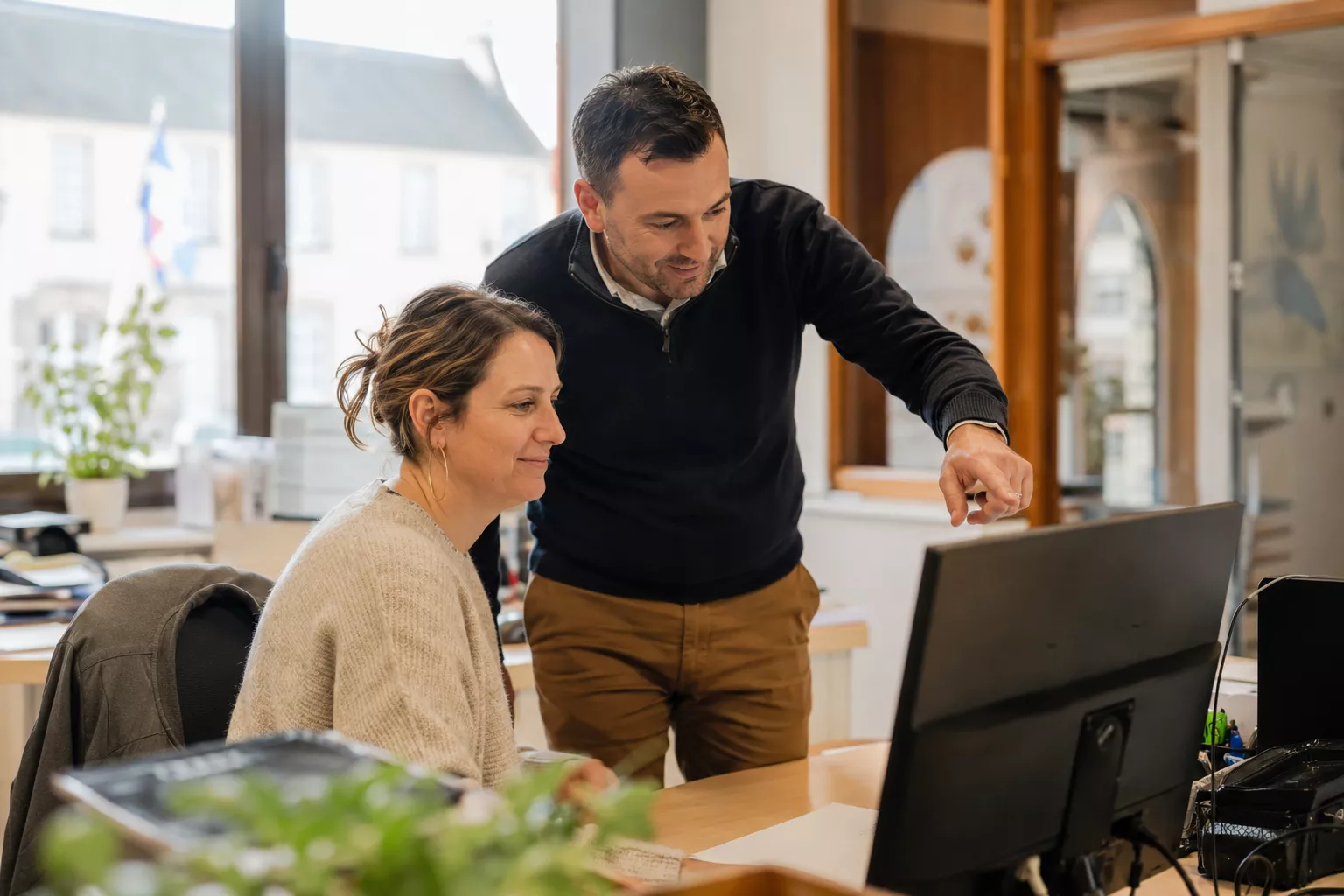 Deux agents d’une collectivité locale travaillent ensemble devant un ordinateur dans un bureau municipal lumineux, avec une ambiance chaleureuse et professionnelle représentative des mairies françaises