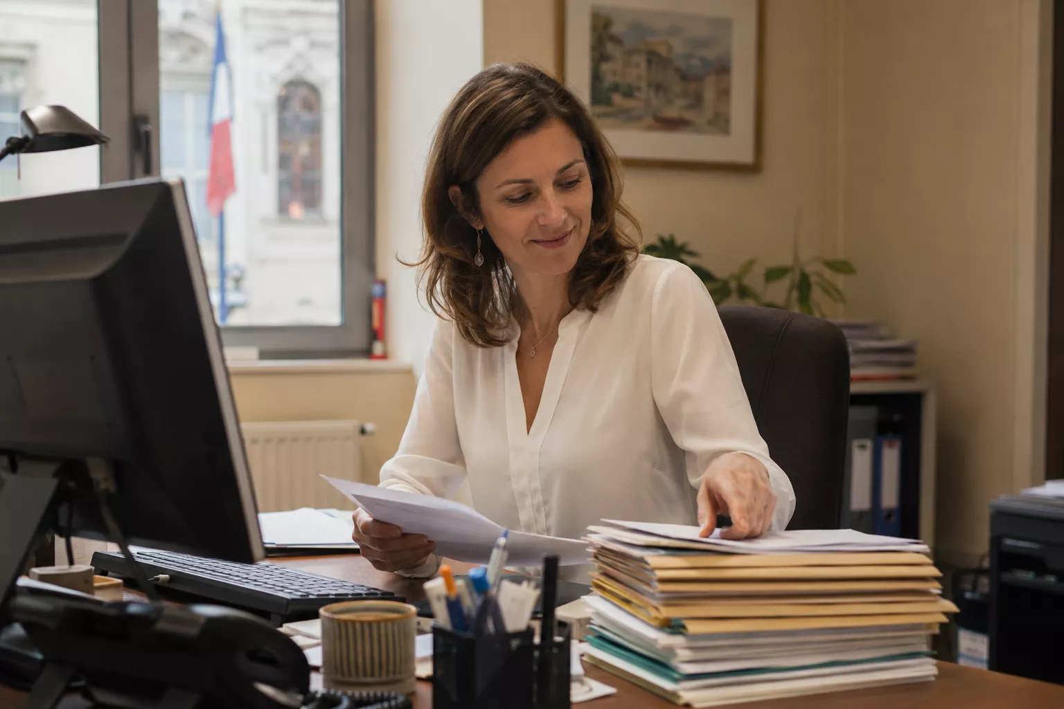 Secrétaire de mairie traitant des courriers et dossiers administratifs dans un bureau de collectivité territoriale moderne.